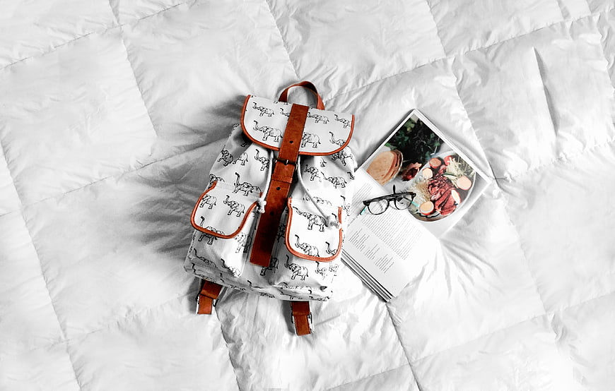 Flat lay of white elephant print backpack with book and glasses