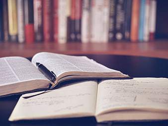 Open Bible and Notebook on Desk with Bookshelf Background