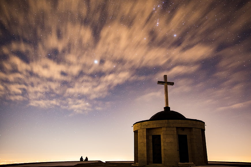 Silhouette of a chapel with cross under starry night sky