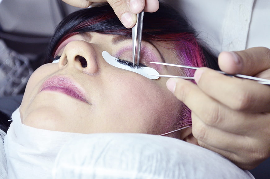 Close-up of eyelash extension application on woman with pink hair