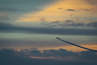 Airplane with smoke trail flying through sunset clouds