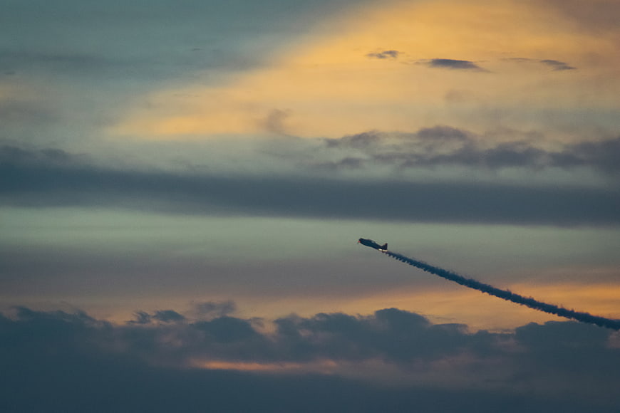 Airplane with smoke trail flying through sunset clouds