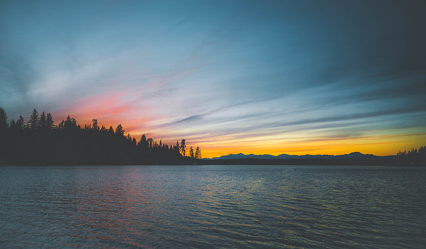 Serene Sunset Over Lake with Silhouetted Forest and Mountains