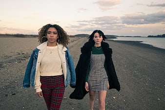 Two Fashionable Women Walking On A Gravel Beach At Dusk