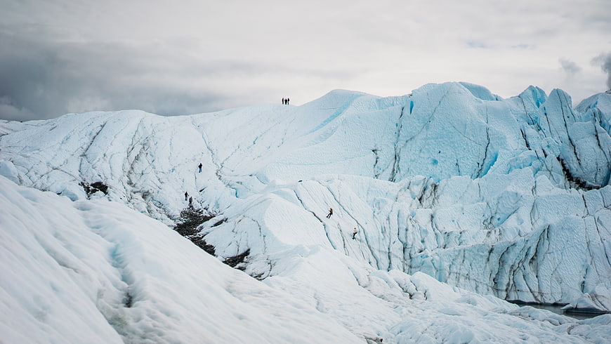 Hikers climbing a massive blue glacier landscape