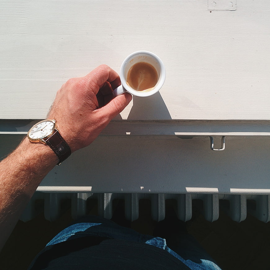 Man's hand holding espresso cup on white railing