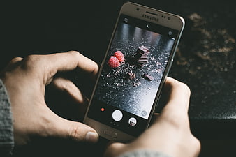 Hands holding smartphone photographing chocolate and raspberries