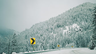 Snowy Mountain Road with Yellow Curve Warning Signs