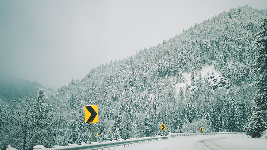Snowy Mountain Road with Yellow Curve Warning Signs