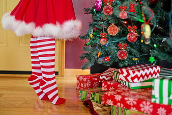 Woman in Santa Skirt and Striped Socks by Christmas Tree