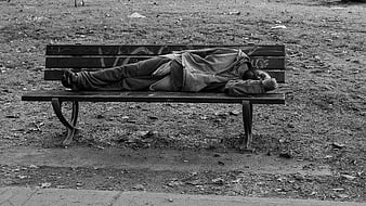 Black and white photo of homeless man sleeping on park bench