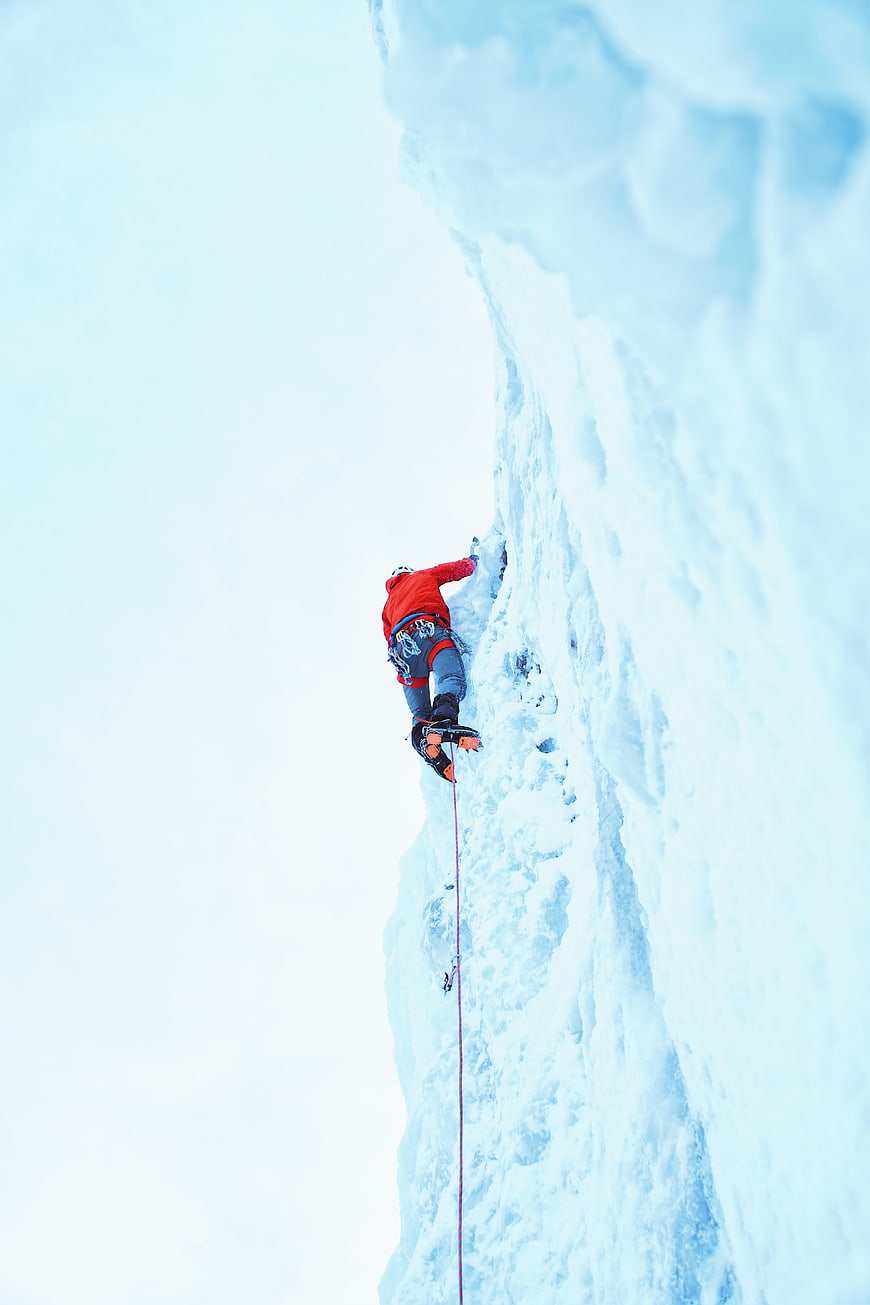 Ice Climber Scaling Vertical Frozen Waterfall in Red Jacket