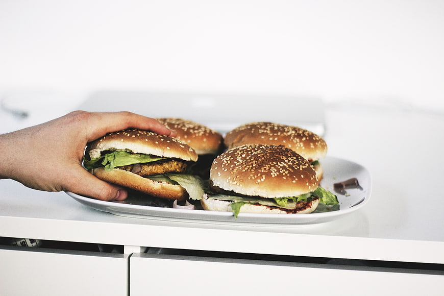 Hand Picking Up Burger from White Plate