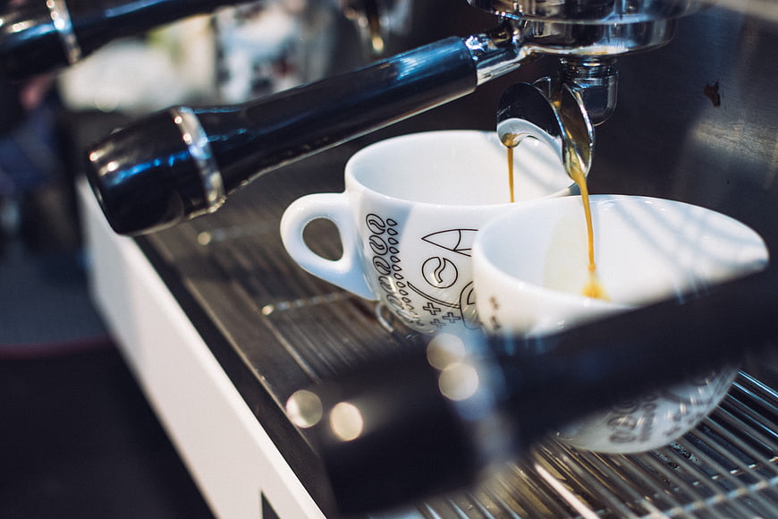 Espresso pouring into white cups from machine