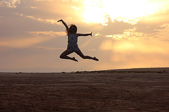 Woman jumping in silhouette against golden sunset sky