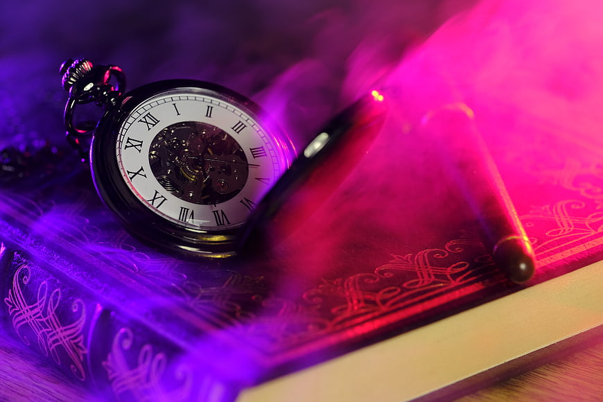 Antique pocket watch and pen on book with purple smoke