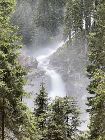 Misty waterfall cascading through a dense evergreen forest landscape