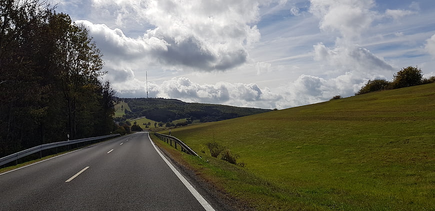 Winding country road through green hills under cloudy sky