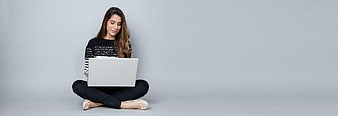 Young woman sitting cross-legged with laptop on gray background
