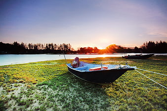 Small wooden boat on grassy shore at sunrise