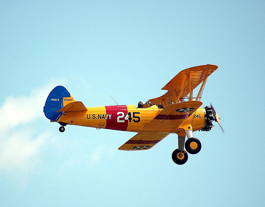 Vintage U.S. Navy Biplane Flying in Blue Sky