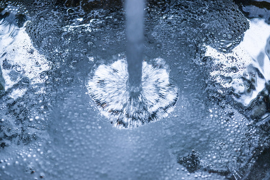 Close-up of water stream splashing into blue liquid with bubbles