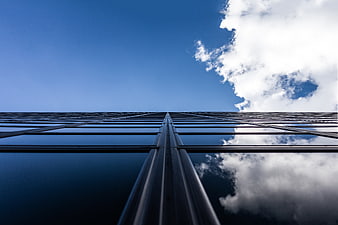 Low angle view of modern glass skyscraper reflecting blue sky and clouds