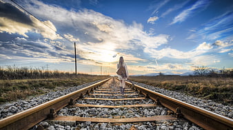 Woman with Guitar Walking on Railroad Tracks at Sunset