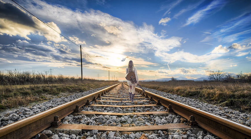Woman with Guitar Walking on Railroad Tracks at Sunset