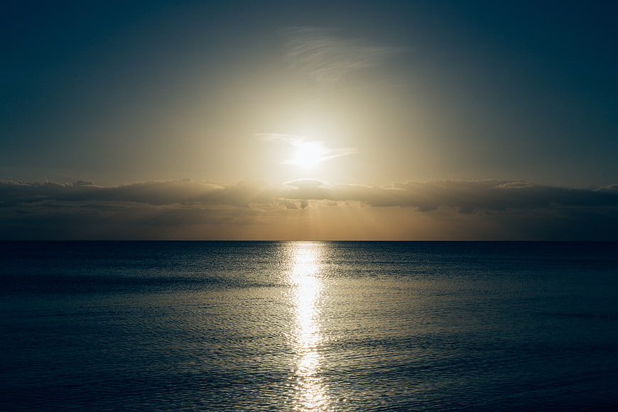 Sunlight reflecting on calm ocean horizon with clouds