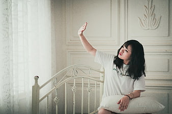 Young Woman Sitting on Bed Reaching Hand Up Indoors
