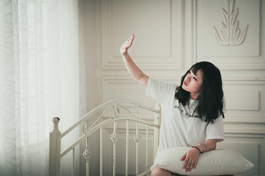 Young Woman Sitting on Bed Reaching Hand Up Indoors