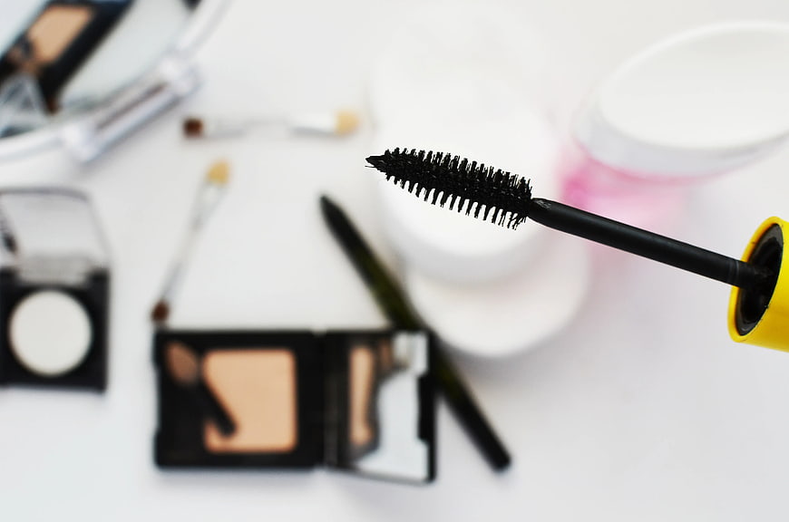 Close-up of mascara wand with blurred makeup background