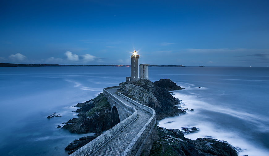 Lighthouse on Rocky Coast with Stone Causeway at Dusk