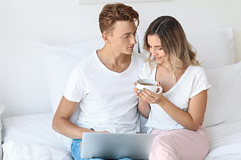 Young couple relaxing on bed with laptop and coffee