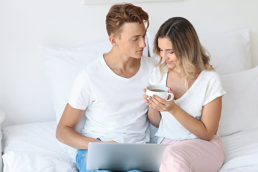 Young couple relaxing on bed with laptop and coffee