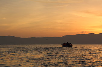 Silhouette of boat with people on ocean at sunset