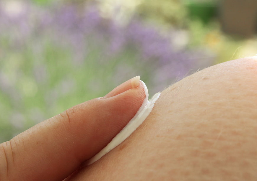 Close-up of hand applying white sunscreen cream to skin outdoors