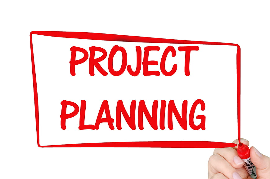 Hand writing project planning in red marker on whiteboard