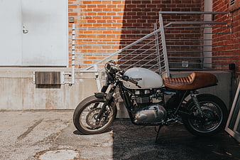 White Triumph Cafe Racer Motorcycle Parked Against Brick Wall