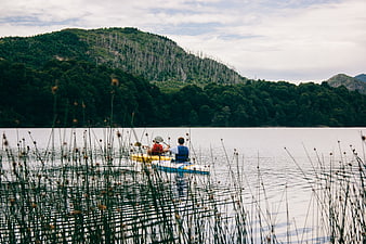 Two people kayaking on a calm lake with forested mountains