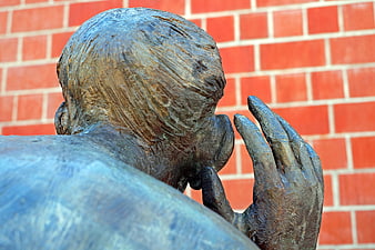 Bronze Sculpture of Man Whispering Against Red Brick Wall