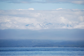Snow-capped mountains emerging from clouds over ocean