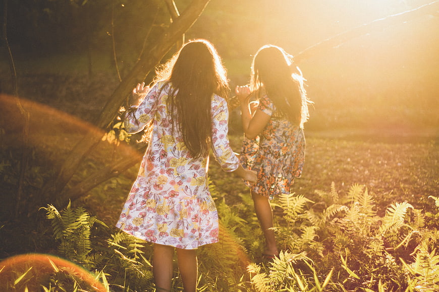 Two Girls Holding Hands Walking in Sunlit Forest