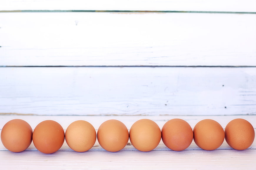 Row of Brown Eggs on White Wooden Background
