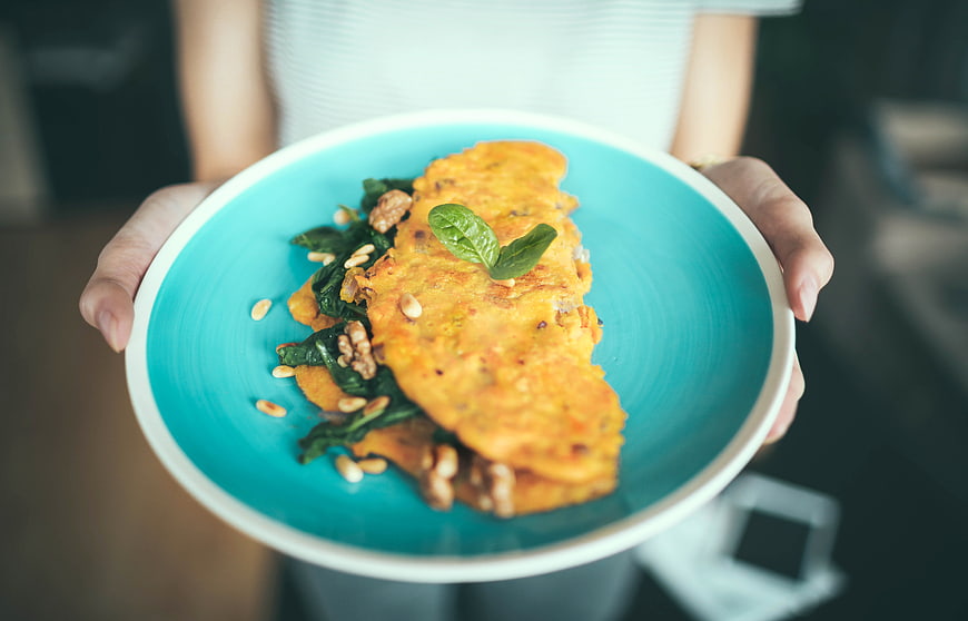 Hands holding a blue plate with savory omelet and spinach