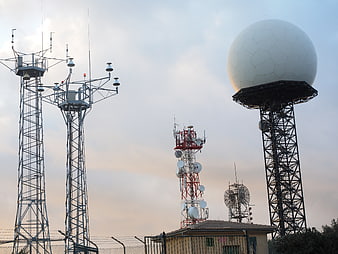 Radar dome and communication towers against cloudy sky
