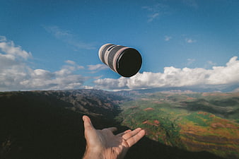 Hand tossing camera lens against mountain landscape