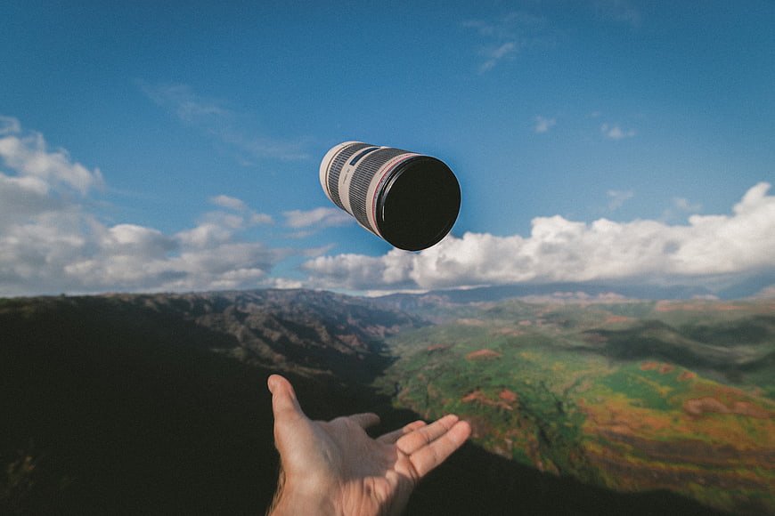 Hand tossing camera lens against mountain landscape