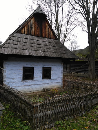 Traditional wooden house with shingle roof and wattle fence